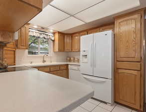 Kitchen featuring light countertops, white appliances, light tile patterned floors, and brown cabinetry