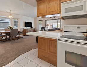 Kitchen featuring white appliances, open floor plan, light carpet, brown cabinetry, and light countertops