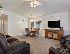 Carpeted living room with vaulted ceiling, a ceiling fan, and a chandelier