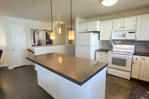 Kitchen featuring white appliances, backsplash, dark wood-style flooring, and a center island