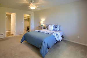 Bedroom with light carpet, connected bathroom, ceiling fan, and a walk in closet