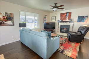 Living area featuring a tile fireplace, dark wood-style flooring, and a ceiling fan