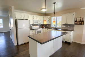 Kitchen featuring pendant lighting, white appliances, dark countertops, and white cabinets