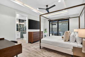 Bedroom featuring a tray ceiling, wood finished floors, ceiling fan, access to outside, and ensuite bath