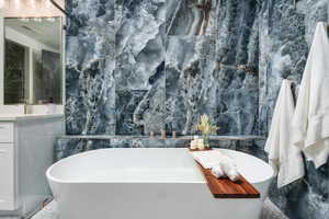 Full bath featuring a freestanding tub, tile walls, and vanity