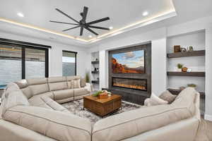 Living area featuring built in features, a tray ceiling, a fireplace, recessed lighting, and a ceiling fan
