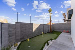 Fenced backyard featuring an area to practice putting and a patio area