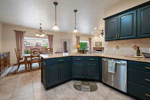 Kitchen with stainless steel dishwasher, tasteful backsplash, a peninsula, decorative light fixtures, and light stone counters