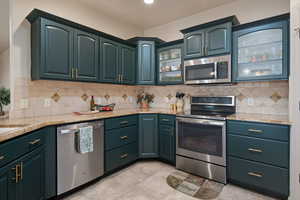 Kitchen with glass insert cabinets, appliances with stainless steel finishes, decorative backsplash, and light stone counters