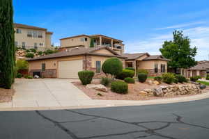 View of front of property with stucco siding, driveway, a balcony, and stone siding