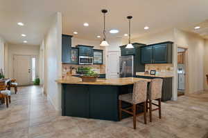 Kitchen featuring pendant lighting, glass insert cabinets, a peninsula, appliances with stainless steel finishes, and a kitchen bar