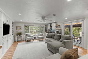 Living room with light wood finished floors, ornamental molding, recessed lighting, a textured ceiling, and ceiling fan