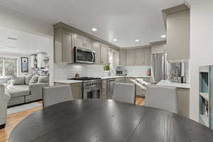 Kitchen with tasteful backsplash, appliances with stainless steel finishes, gray cabinets, light stone counters, and recessed lighting