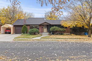 Mid-century home featuring a chimney, driveway, a shingled roof, brick siding, and an attached garage