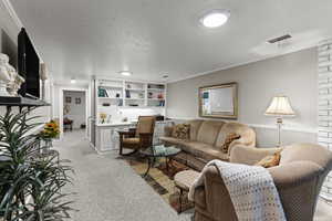Living area with a textured ceiling, light carpet, ornamental molding, and built in desk