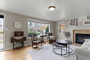 Living room featuring light wood-style flooring, a tiled fireplace, a textured ceiling, and ornamental molding