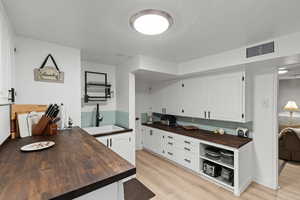 Kitchen with white cabinets, wooden counters, light wood finished floors, backsplash, and a textured ceiling