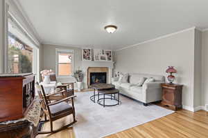 Living area featuring a tiled fireplace, ornamental molding, light wood-style flooring, and a textured ceiling