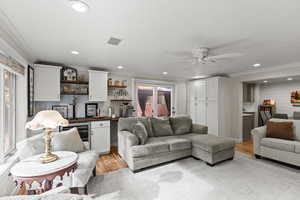 Living area featuring bar with sink, ornamental molding, light wood-style floors, recessed lighting, and wine cooler