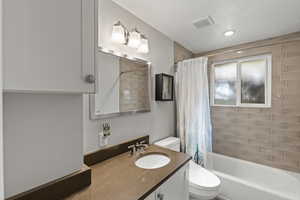 Full bathroom featuring shower / bathtub combination with curtain, vanity, and a textured ceiling