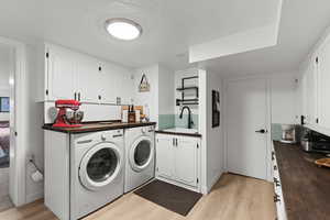 Washroom with a textured ceiling, light wood finished floors, washing machine and clothes dryer, and cabinet space