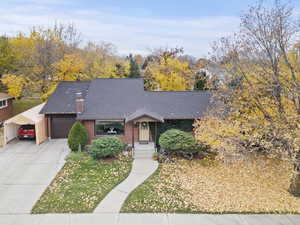 Mid-century inspired home with driveway, brick siding, a shingled roof, a chimney, and a garage