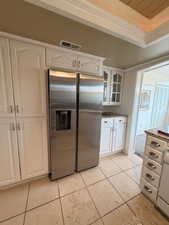 Kitchen with stainless steel refrigerator with ice dispenser, white cabinetry, light tile patterned floors, crown molding, and glass insert cabinets