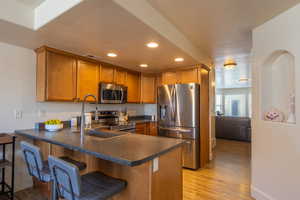 Kitchen featuring appliances with stainless steel finishes, recessed lighting, dark countertops, brown cabinetry, and light wood-type flooring