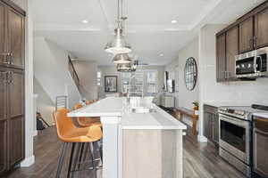 Kitchen featuring beamed ceiling, a kitchen breakfast bar, appliances with stainless steel finishes, decorative light fixtures, and dark wood finished floors