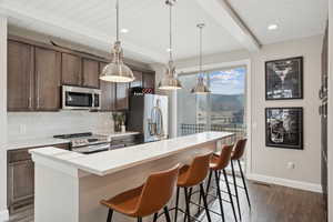 Kitchen featuring beam ceiling, decorative backsplash, pendant lighting, dark wood-style flooring, and a breakfast bar area