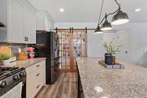 Kitchen with a barn door, white cabinets, dark wood finished floors, decorative light fixtures, and recessed lighting