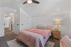 Bedroom with dark colored carpet, lofted ceiling, a closet, and ceiling fan