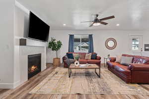 Living area featuring wood finished floors, a textured ceiling, a tile fireplace, a ceiling fan, and recessed lighting