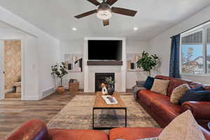 Living room featuring wood finished floors, a lit fireplace, ceiling fan, recessed lighting, and a textured ceiling