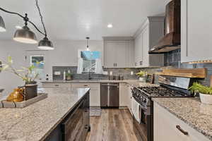 Kitchen with stainless steel appliances, wall chimney exhaust hood, hanging light fixtures, light wood-type flooring, and a textured ceiling