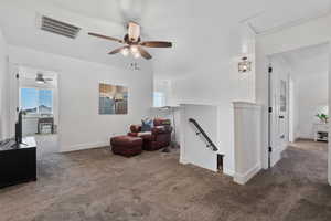 Living area with an upstairs landing, carpet, and a ceiling fan