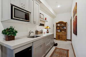 Kitchen with stainless steel microwave, gray cabinets, light stone countertops, light colored carpet, and open shelves