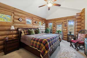 Carpeted bedroom featuring high vaulted ceiling, access to outside, a ceiling fan, and log walls