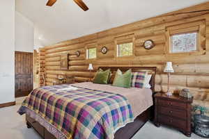 Bedroom with carpet floors, ceiling fan, vaulted ceiling, log walls, and wooden walls