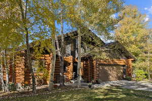 Log cabin featuring log siding, driveway, and an attached garage