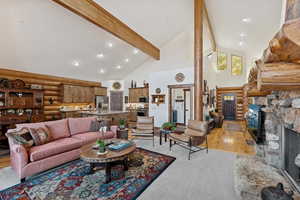 Living room featuring log walls, high vaulted ceiling, light wood-type flooring, beam ceiling, and a stone fireplace