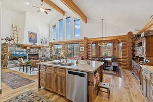 Kitchen with high vaulted ceiling, stainless steel dishwasher, open floor plan, light stone counters, and pendant lighting
