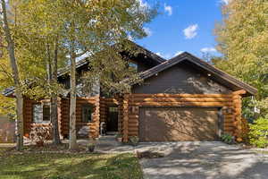Log-style house with log siding, concrete driveway, and a garage