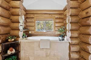 Bathroom featuring lofted ceiling, a garden tub, and rustic walls