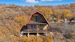 Rear view of property featuring a view of trees, a deck, and a gambrel roof