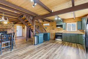 Kitchen with rail lighting, a wooden ceiling with exposed beams, light wood-style flooring, green cabinetry, and wood walls