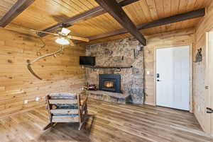 Living area featuring wood walls, a wood ceiling with exposed beams, wood finished floors, a wood stove, and ceiling fan