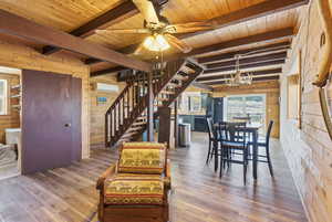 Dining space with wooden walls, stairway, a chandelier, wood finished floors, and a ceiling fan