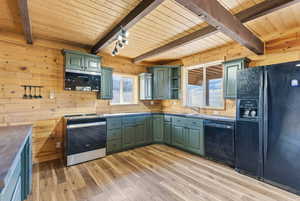 Kitchen with black appliances, green cabinetry, wood walls, light wood-type flooring, and a wooden ceiling with exposed beams