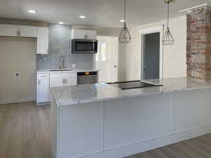 Kitchen with light stone countertops, a peninsula, light wood-style flooring, appliances with stainless steel finishes, and recessed lighting